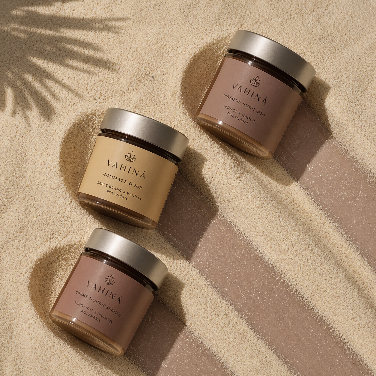 rituel de soins naturels Vahina avec gommage, masque et crème posés sur sable évoquant une routine sensorielle inspirée de la Polynésie