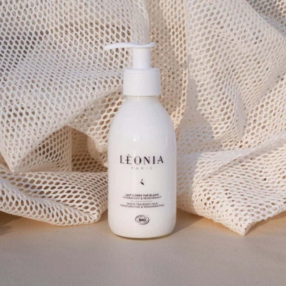 Visuel du Lait Corps Thé Blanc Léonia Paris avec flacon posé près d’une texture fondante sur textile clair, dans une ambiance soin corps sensorielle.