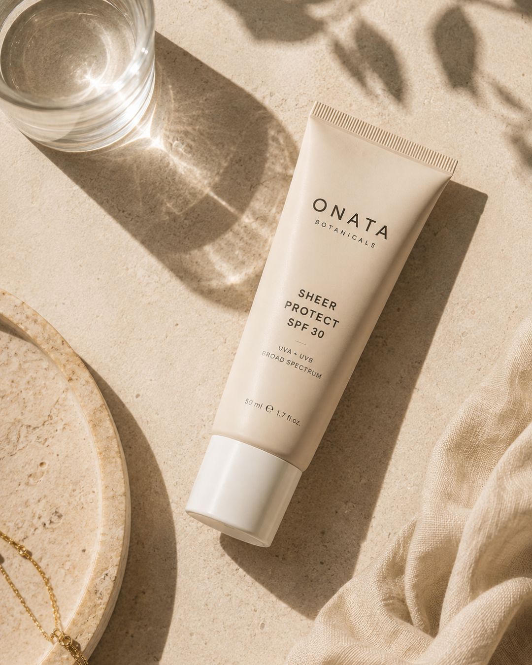 Tube de protection solaire SPF posé en flat lay sur une surface beige texturée, dans une composition minimaliste baignée de lumière naturelle avec des ombres douces et une ambiance premium.